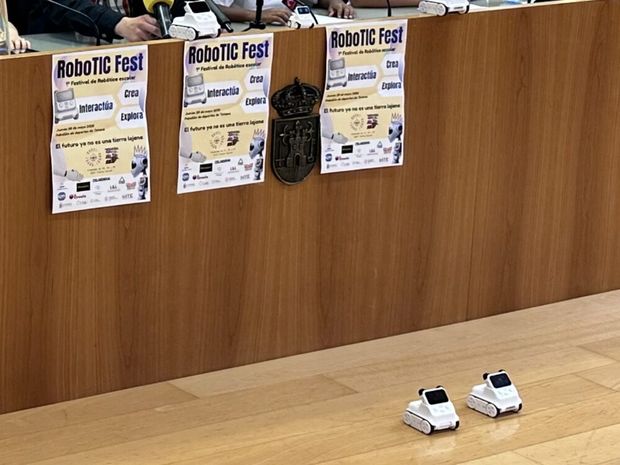 Carteles del RoboTIC Fest y robots educativos sobre la mesa del pleno